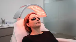 A woman is getting a facial treatment with red LED light therapy in a clinic.