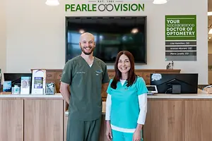 A man and woman standing at a reception desk in a Pearle Vision eye care clinic.