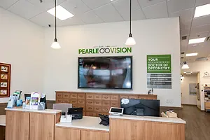 An indoor photo of the Centennial Pearle Vision, a store with a reception desk and a mounted TV displaying a person wearing glasses.