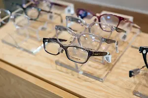 Several pairs of eyeglasses with different colored frames and lenses are displayed on a wooden table in a store.