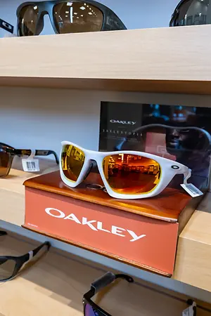 A wooden shelf with a collection of Oakley sunglasses on display, including a pair with yellow lenses and a box with the word Oakley printed on it.