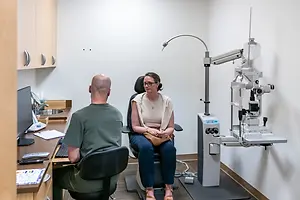 A man and woman are sitting in front of a doctor's desk in an optometrist's office