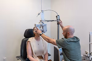 A male optometrist adjusts a machine on a woman's head in an office