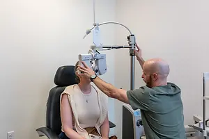 A male optometrist adjusts a machine on a woman's head in an office