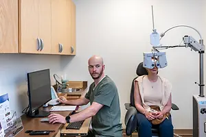 An optometrist is using an ophthalmoscope to check a patient's eyes in a clinic.