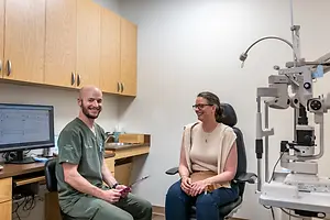 A man and a woman sitting in a chair in a medical office room with a machine behind them