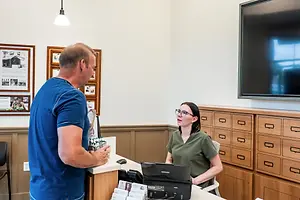 A man wearing a blue shirt and a woman in green scrubs sit at a counter and talk to each other.
