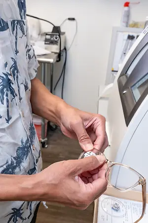 A person is adjusting a pair of glasses in a laboratory or eye care clinic setting.