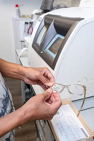 A person is adjusting a pair of glasses in front of a machine in a room.