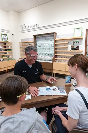 Three people sit around a table in a Centennial eyeglasses shop, with one man smiling and speaking to the other two