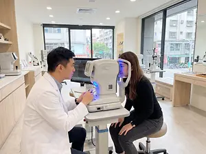 A man in a white lab coat is examining a woman's eyes with a medical device.