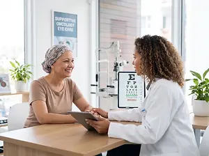 A woman sits at a table with a doctor and uses a tablet to read an eye chart
