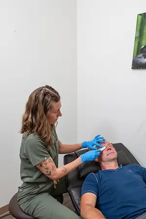A woman in a green outfit is performing a medical procedure on a man wearing a blue shirt