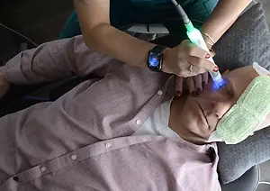 A man lying down on a chair getting his face treated with a blue light