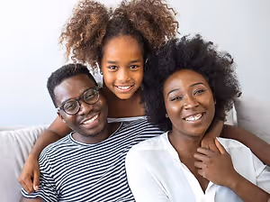 A family of three, a man, a woman, and a girl, sitting on a couch, smiling and posing for a photo