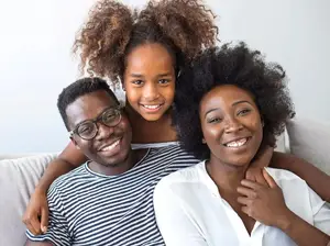 A family of three, a man, a woman, and a girl, sitting on a couch, smiling and posing for a photo