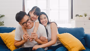 A happy family sitting on a blue couch with yellow pillows in a bright room
