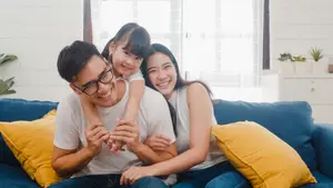 A happy family sitting on a blue couch with yellow pillows in a bright room