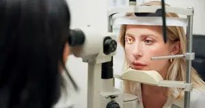 A woman is looking through a machine used for eye examinations.