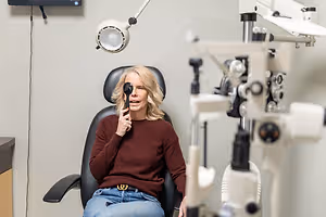 A woman in a maroon sweater is sitting in a chair in an optometrist's office.