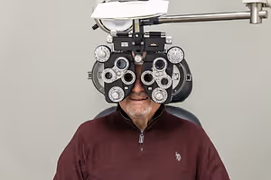 Man in a burgundy sweater undergoing an eye examination with a professional autorefractor