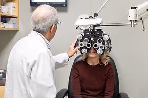 An elderly man, probably an eye doctor, is adjusting the eye machine of a woman who is sitting on a chair.