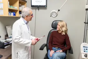 An elderly man in a white coat is talking to a woman in a chair in a clinic