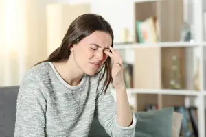 A woman sitting on a couch with her hand on her forehead