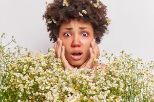A woman with curly hair in a field of flowers with a surprised expression