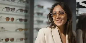 A woman wearing sunglasses and smiling for a photo in front of a display of sunglasses