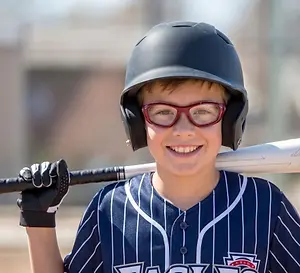 Young boy playing baseball wearing safety sport eyewear holding a baseball bat and wearing a baseball helmet