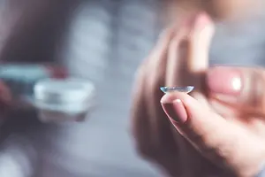 A closeup of a woman with a contact lens in her hand