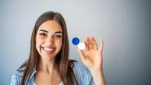 Woman holding a blue and white contact lens bottle and smiling