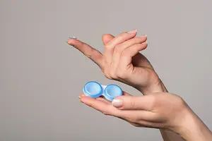 Image of a person's hand holding a blue contact lens in a container