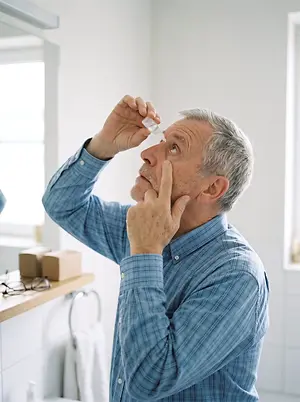 Older man applying eye drops while looking upward