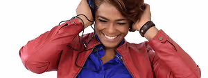 A woman wearing a red jacket and blue shirt is smiling and holding headphones on her head with both hands