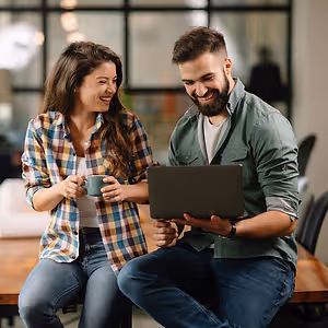 A man and a woman sitting on chairs in front of a table and a laptop