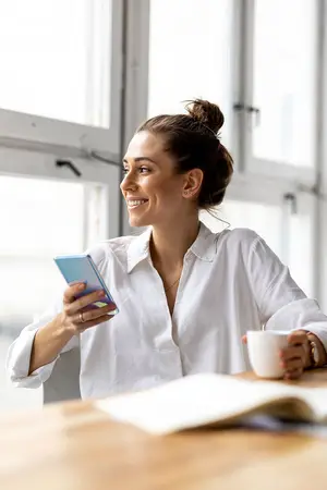 A woman is sitting at a table with a cup of coffee and a phone in her hand