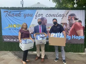 Three people wearing face masks stand next to each other in front of a banner that says Thank You For Coming!
