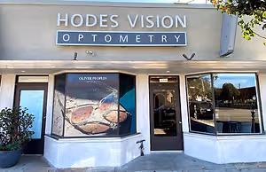 Exterior of the Hodges Vision Optometry Los Angeles store with a glass window displaying sunglasses and a potted plant on the side.