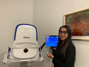 A woman is standing next to a Nikon optos machine in a medical room