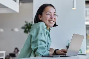 Asian woman in eyeglasses using a laptop in a modern office