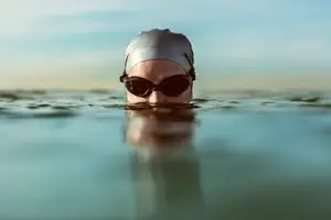 A woman swimming in the sea with a swim cap and goggles on during the day