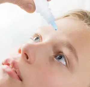 A person administering eye drops to a young girl's eye.