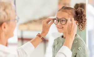 An optometrist is adjusting the glasses on a child in a green sweater.
