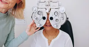 An adult woman is getting her eyes examined by a doctor with an ophthalmoscope in a clinic.