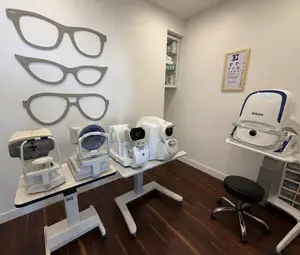 An eye doctor's office with several eye examination machines and a stool, all on a wooden floor.