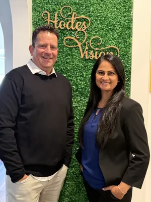 A man and a woman are standing together in front of a wall that says 'Hodes Vision' with a green background.