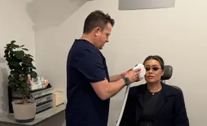 An adult male doctor uses an electric device to treat a seated adult female patient in a clinic.
