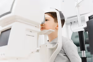 A boy is looking into a machine with a green chair behind him